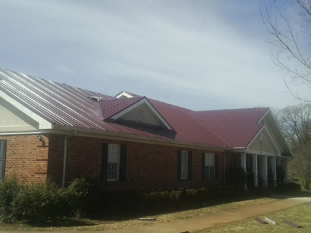 Red metal roof with gabled entries on a long brick building, from a Hail Damage Roof Repair job in Woodstock